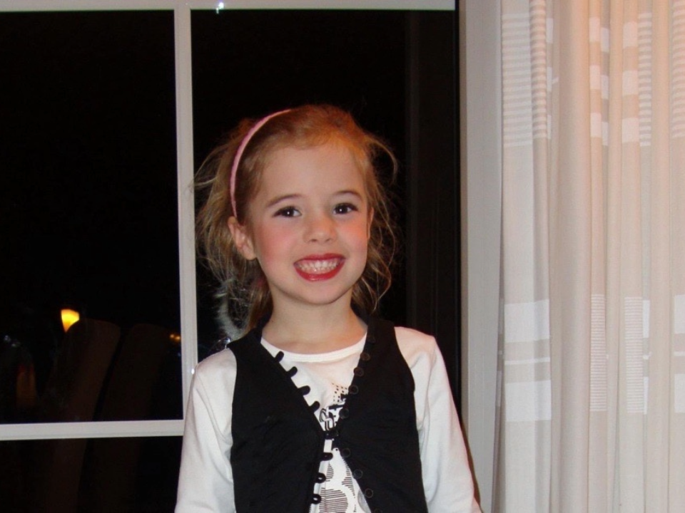 Meisje met een brede glimlach staat binnen voor een raam